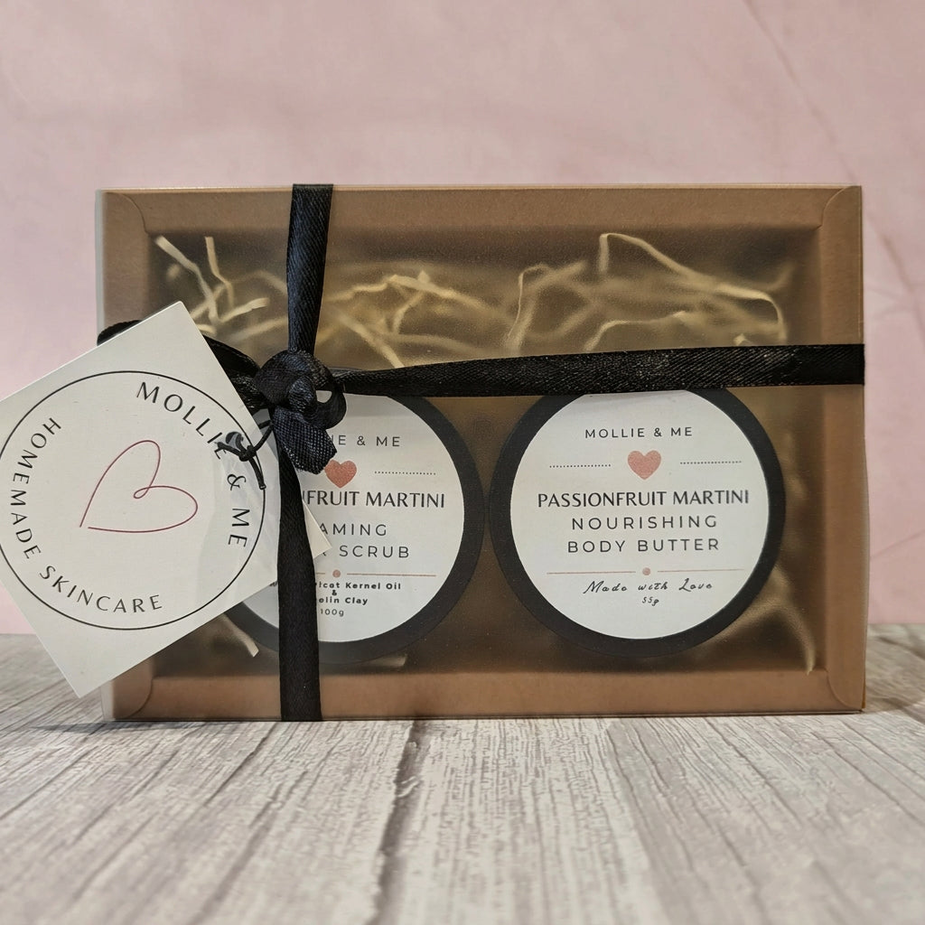 A gift set of two round skincare jars in a kraft paper box with a black ribbon and tag. The products are labeled 'Mollie & Me' and include 'Passionfruit Martini Nourishing Body Butter' and 'Passionfruit Martini Aromatic Body Scrub'. Handmade skincare, made in Kent.