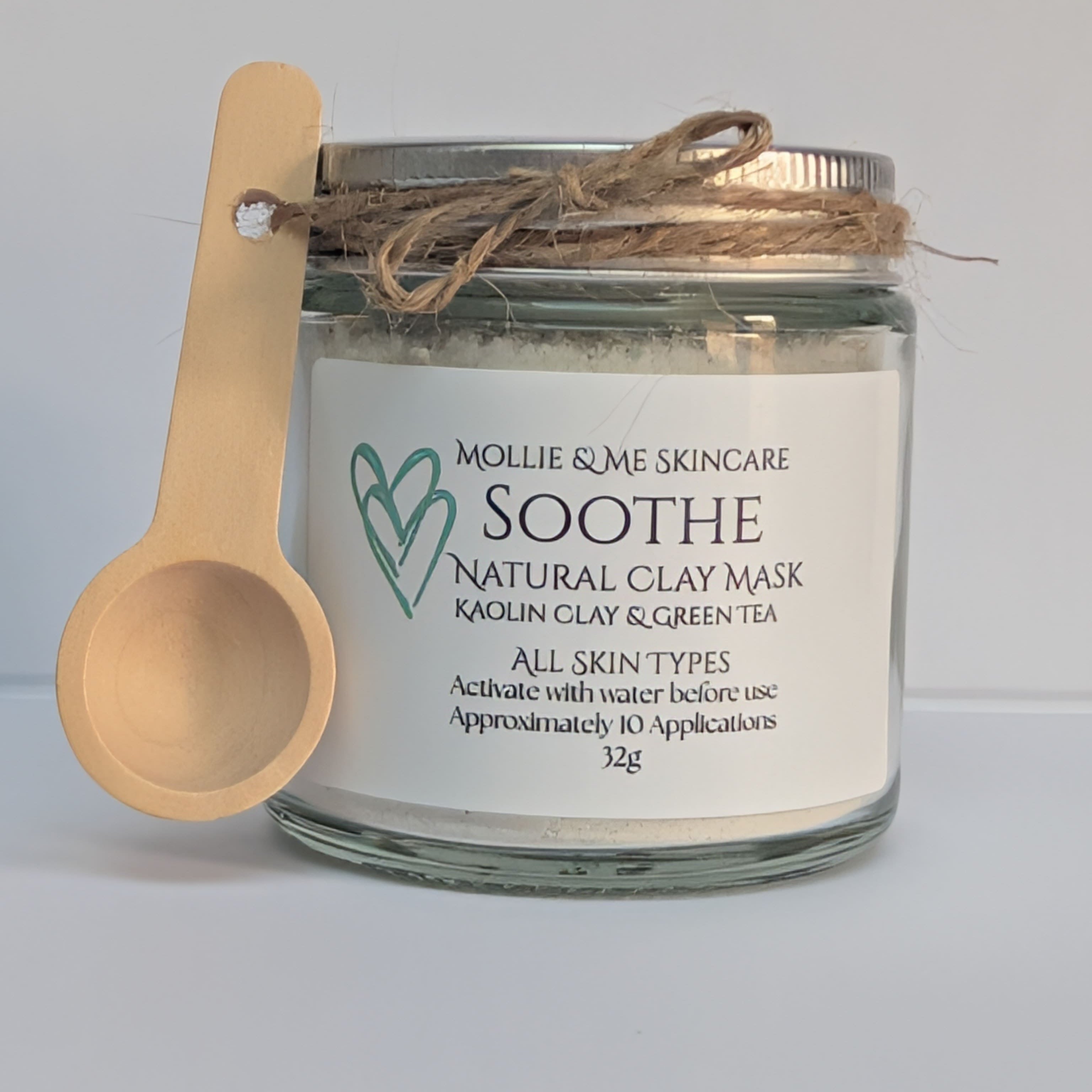 Jar of Mollie & Me Skincare Soothe Natural Clay Mask with a wooden scoop on a light gray background