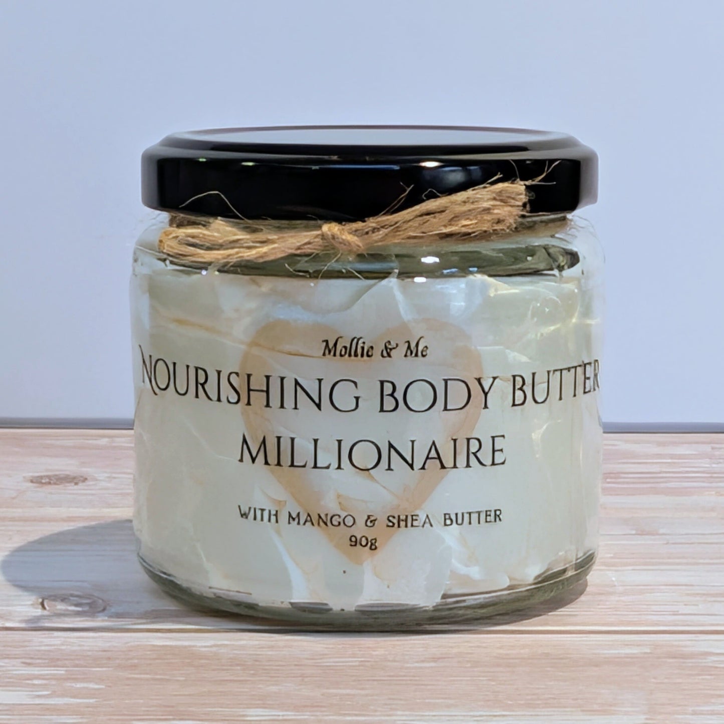 Jar of Mollie & Me Nourishing Body Butter Millionaire on a wooden surface with a light blue background